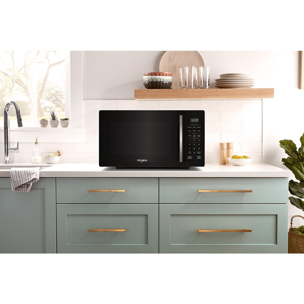 Black microwave with electronic touch controls and LED display on white countertop in kitchen with green cabinetry