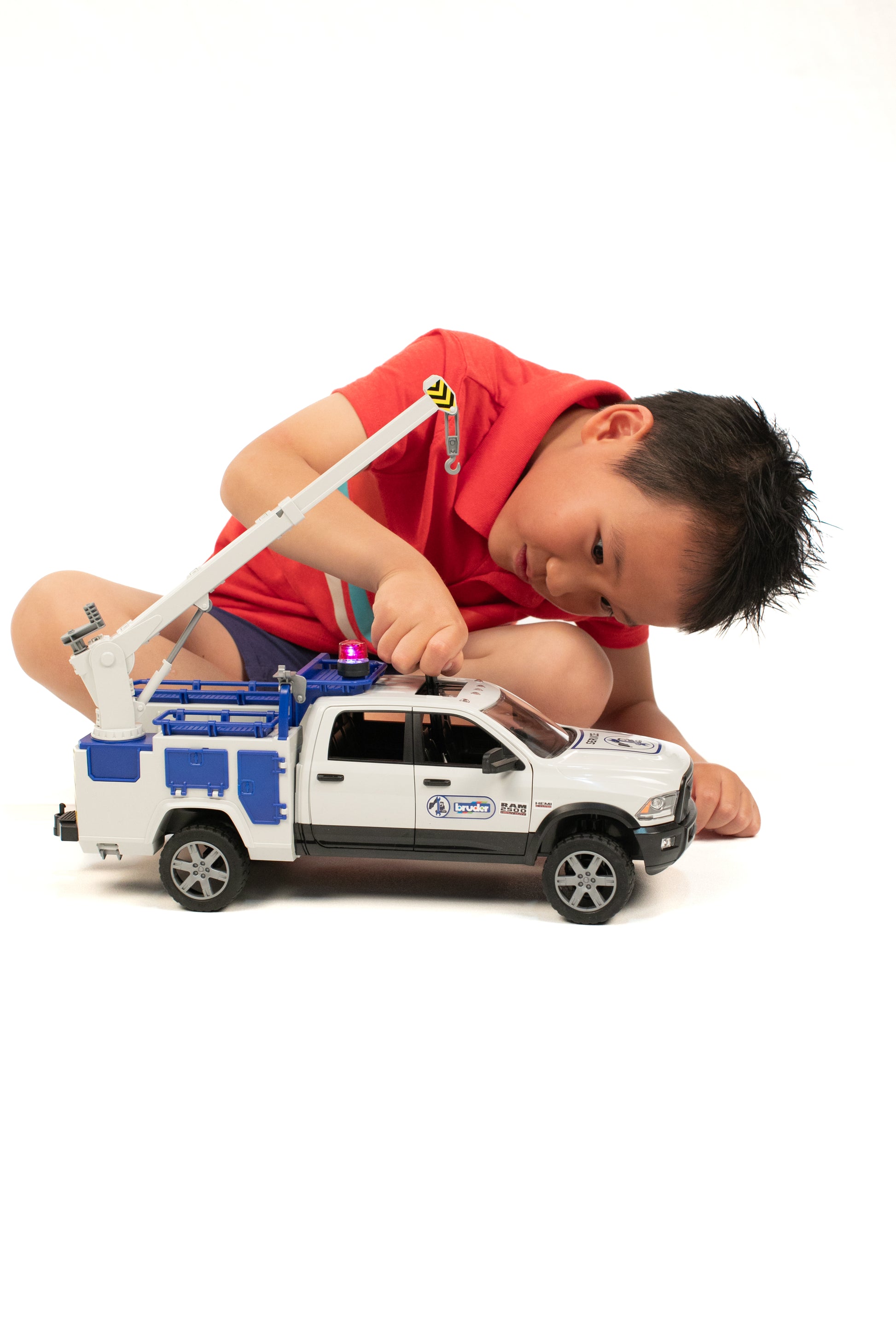 Child in red shirt playing with white and blue Bruder RAM service truck toy featuring crane and working rotating light