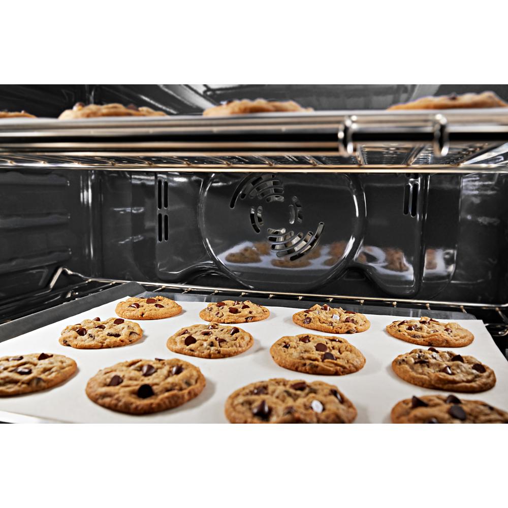 Chocolate chip cookies baking inside a stainless steel microwave combo wall oven with convection fan visible