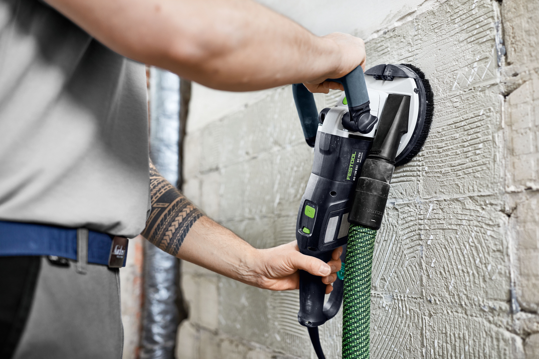 Person operating Festool grinder with dust extraction smoothing wall surface during home improvement tasks
