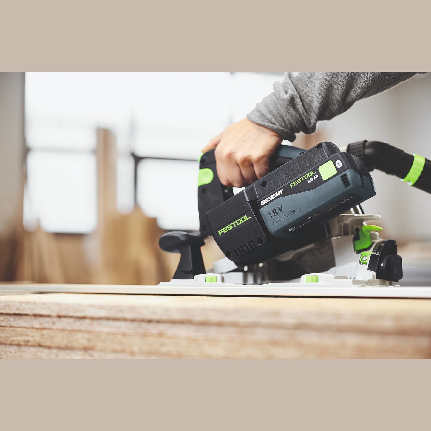 Hand gripping Festool 18V cordless power tool with rechargeable battery working on woodworking project indoors