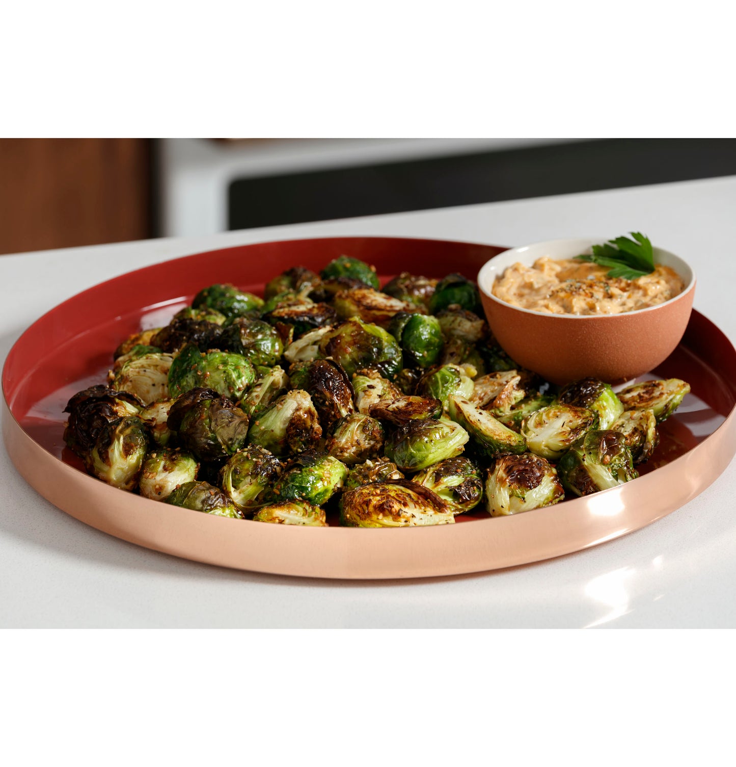 Roasted Brussels sprouts served on a two-toned ceramic plate with a small bowl of dip on white kitchen countertop