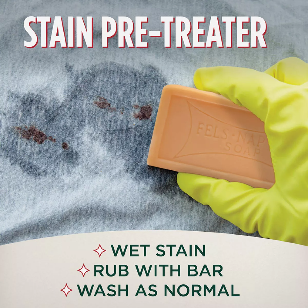 Hand applying orange laundry soap bar to blue fabric with rust-colored stains using yellow glove for stain removal