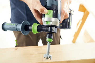 Person holding a Festool cordless hammer drill with side handle preparing to drill wood during home improvement task