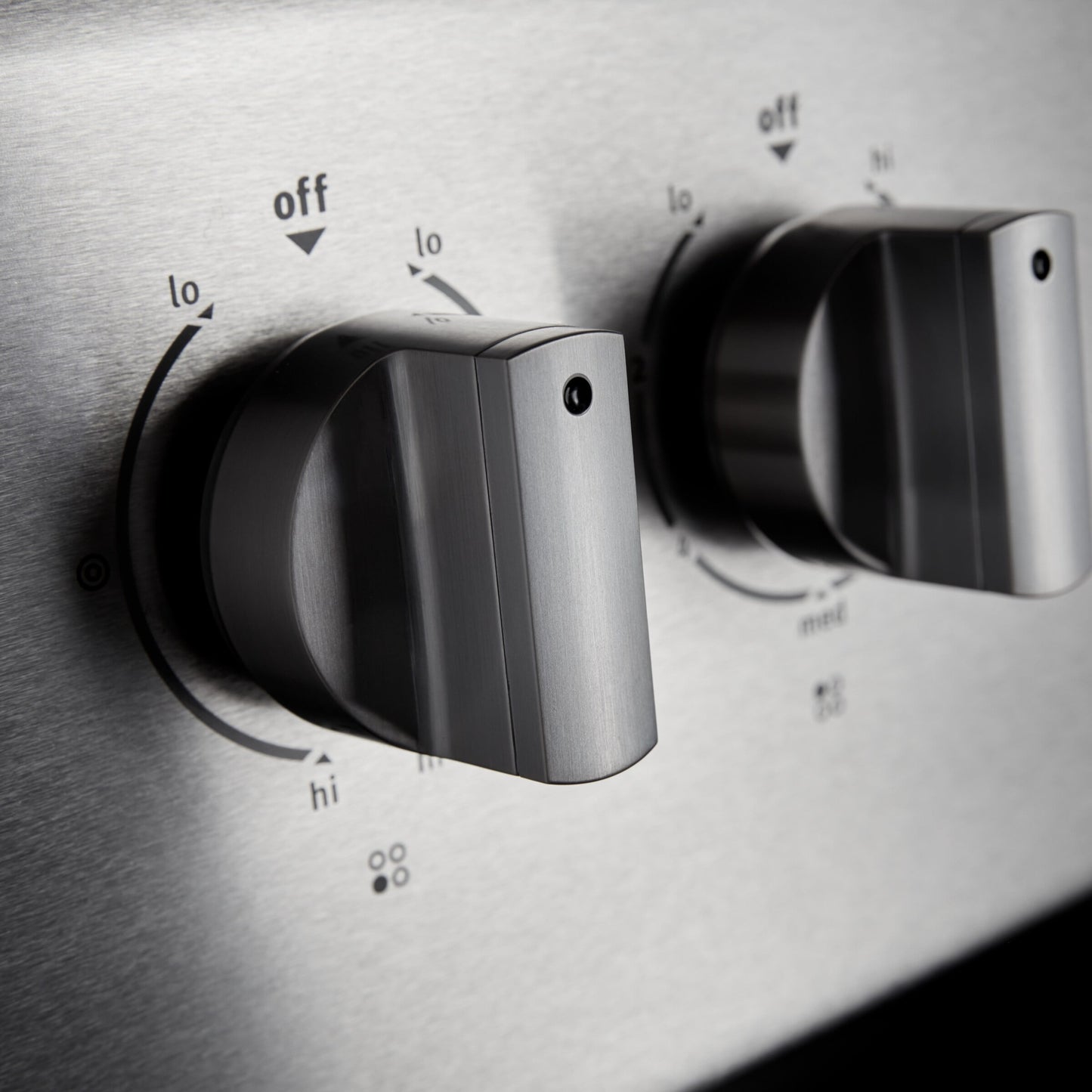 Close-up of stainless steel electric range control knobs with temperature settings from low to high for home appliances.