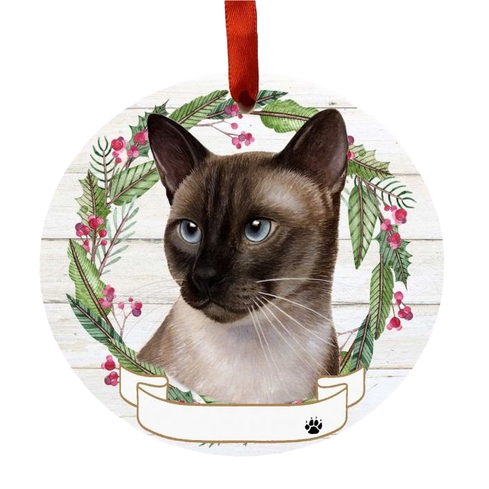 Round Christmas ornament featuring a Siamese cat face framed by a holly and greenery wreath with red ribbon hanger
