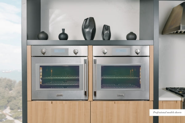 Two stainless steel single wall ovens with digital displays and control knobs, built into modern wood cabinetry