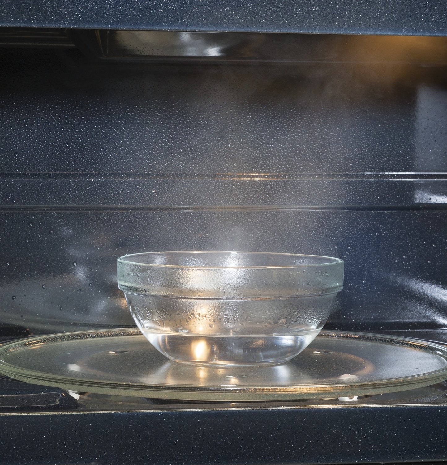 Clear glass bowl with water steaming inside an over-the-range microwave, part of Kitchen & Kitchenware collection
