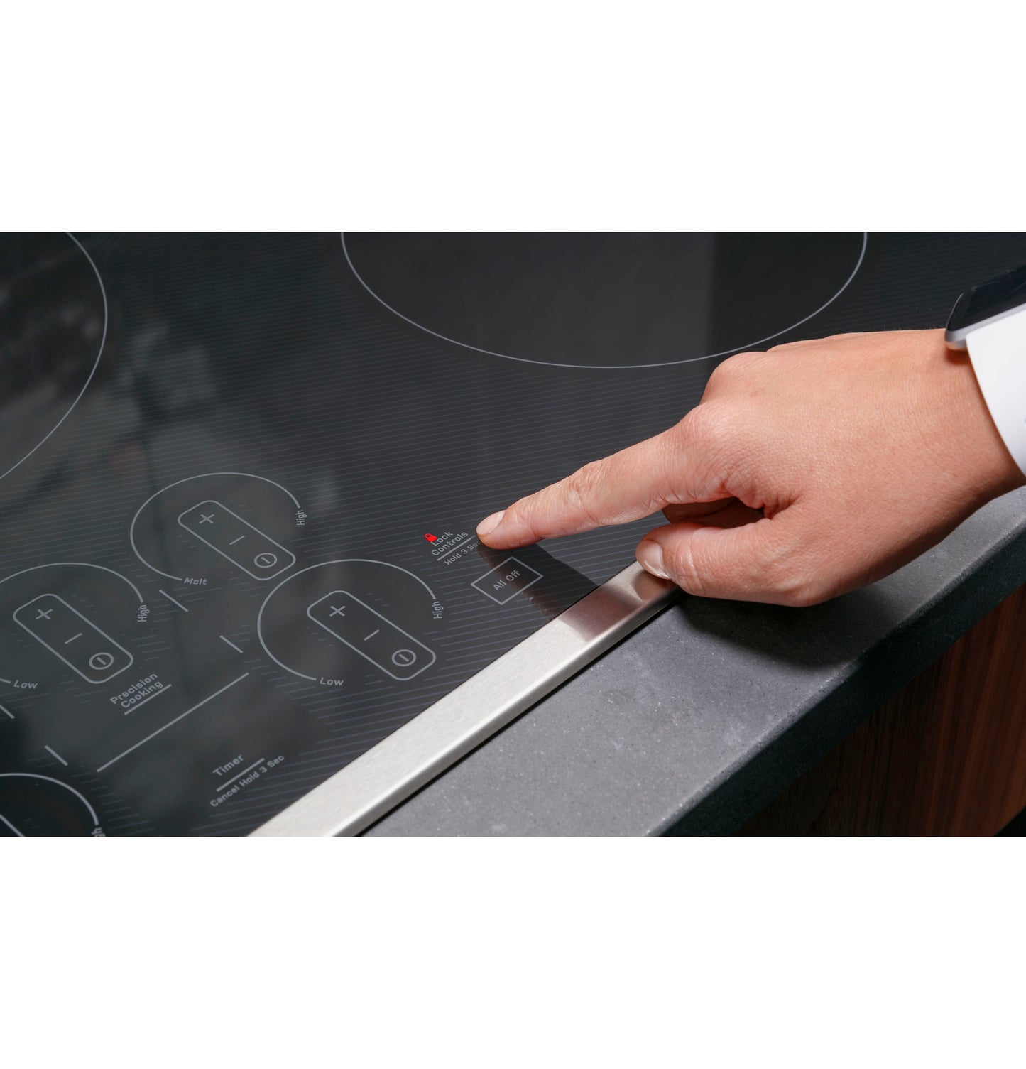 Finger pressing touch control panel on black glass induction cooktop in modern kitchen with wood cabinets and stone countertop
