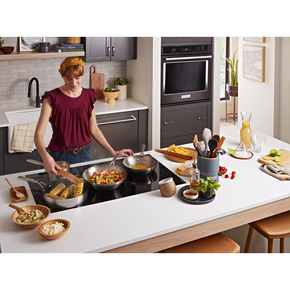 Woman cooking on sleek black induction cooktop with five elements in modern kitchen and cookware setup