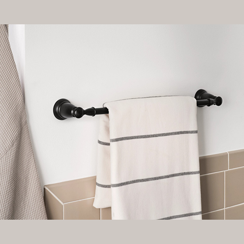 Matte black metal towel bar with decorative end mounts holding a white towel with gray stripes above beige tile wall