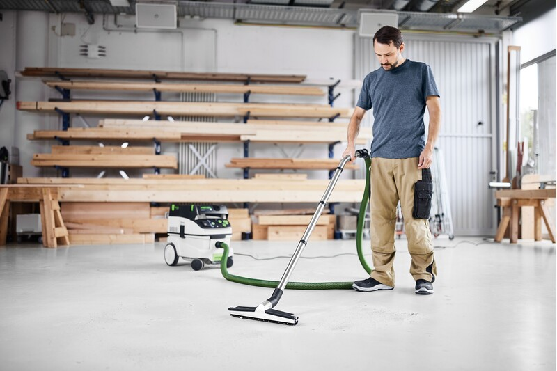 Man using a dust extractor with flexible hose in a woodworking shop for dust collection and home improvement tasks