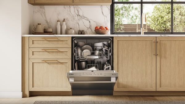 Open stainless steel dishwasher filled with clean dishes in a modern kitchen with wood cabinetry and marble backsplash