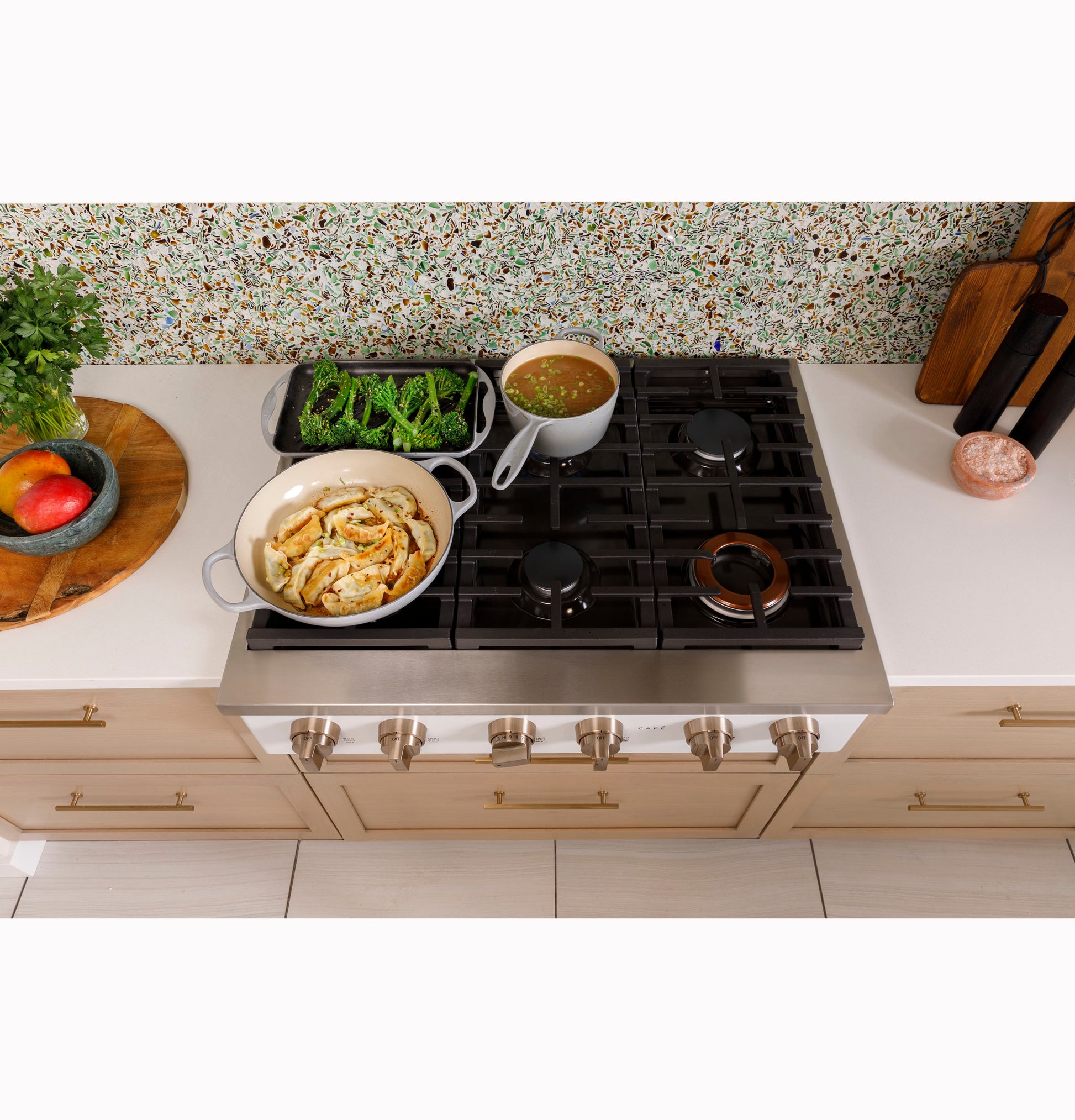 36-inch commercial-style stainless steel gas rangetop with six burners cooking vegetables and sauce in modern kitchen