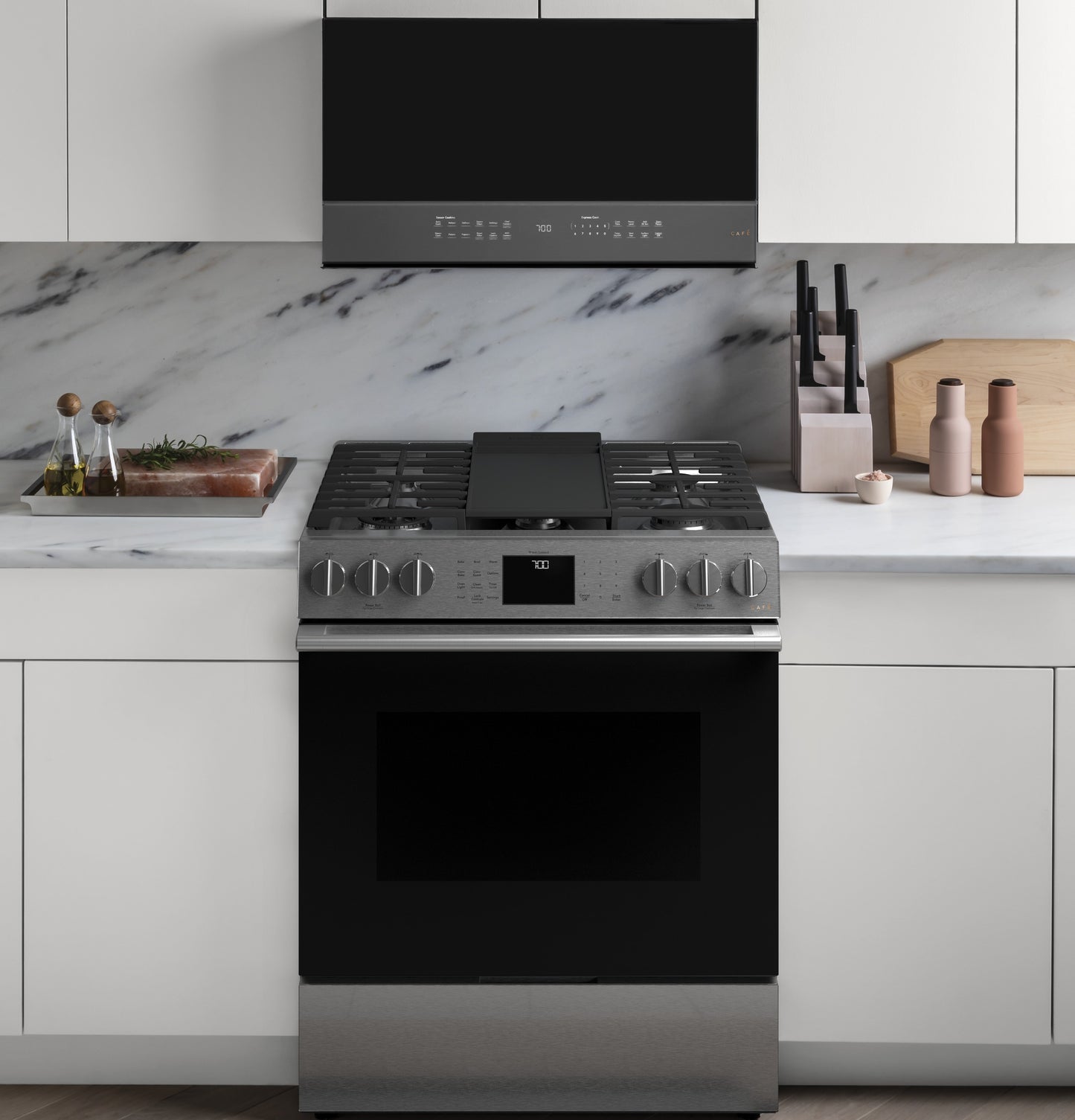 Stainless steel slide-in gas range with convection oven, digital display, and black vent hood in modern kitchen setting