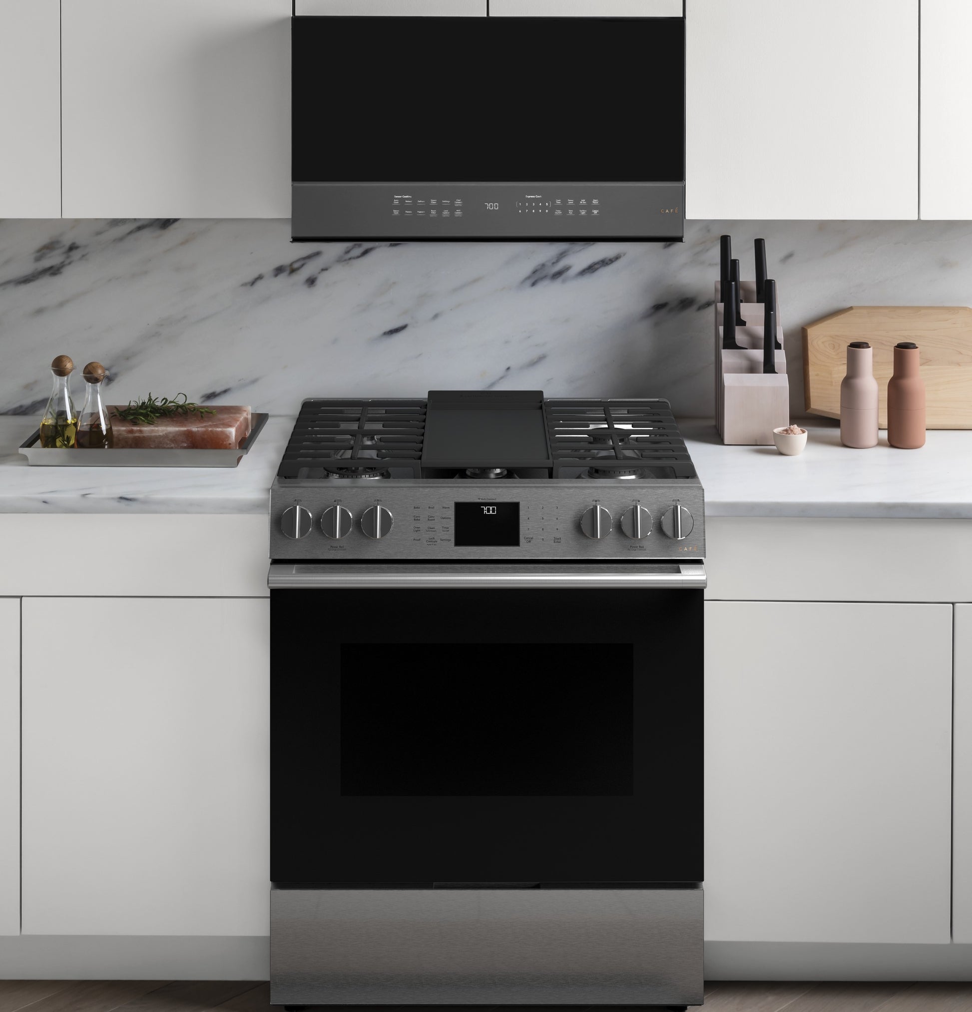 Stainless steel slide-in gas range with convection oven, digital display, and black vent hood in modern kitchen setting