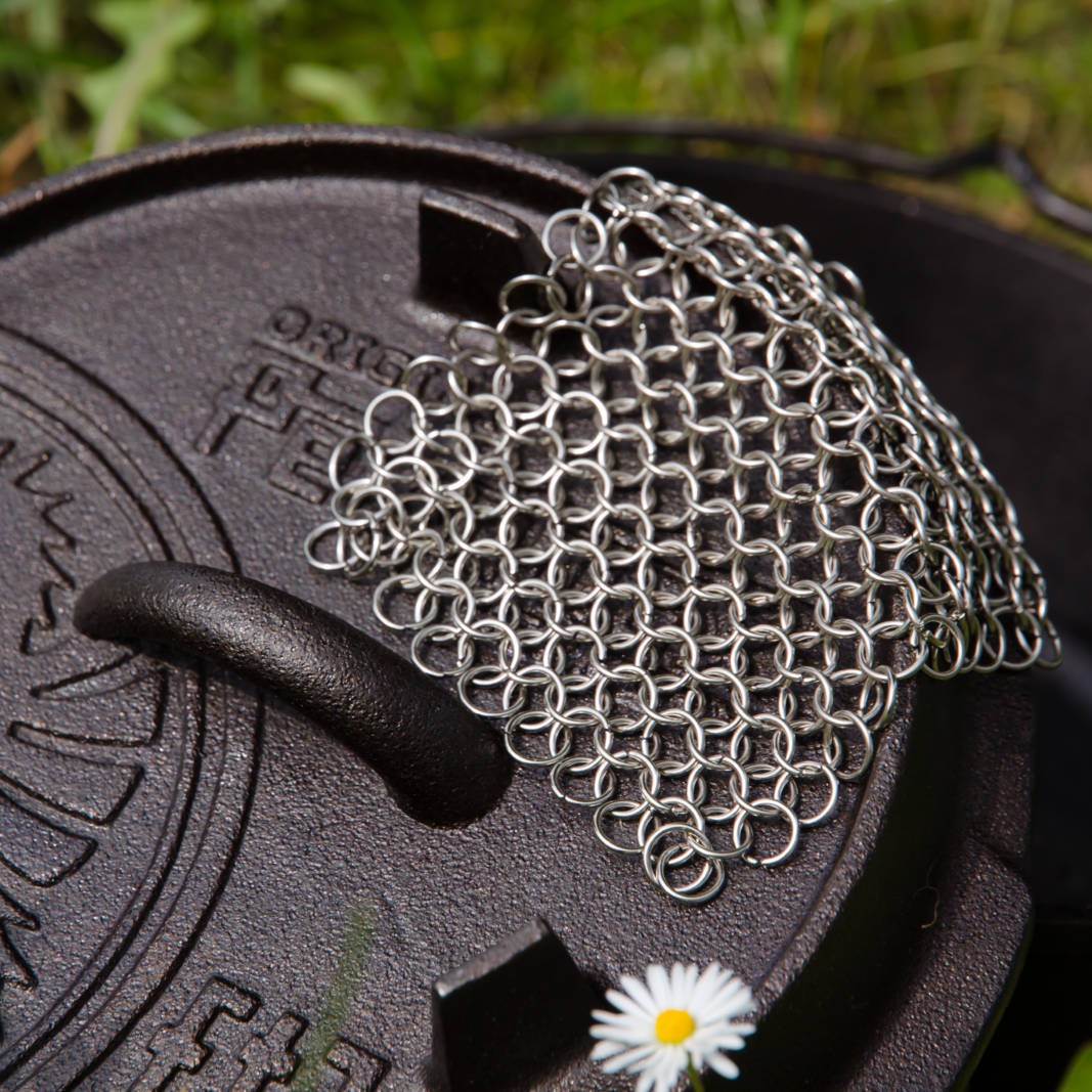 Stainless steel chainmail scrubber resting on cast iron cookware lid outdoors in kitchenware collection under $50 tools