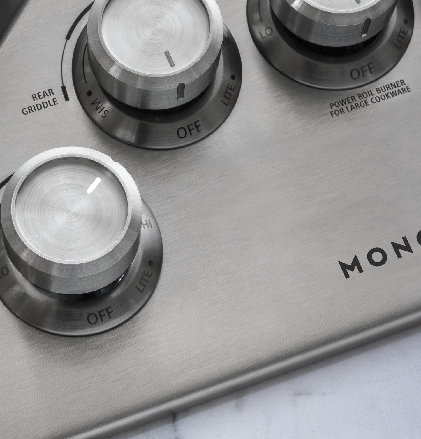 Close-up of brushed stainless steel gas cooktop control knobs with labels for rear griddle and power boil burner in kitchen appliances collection