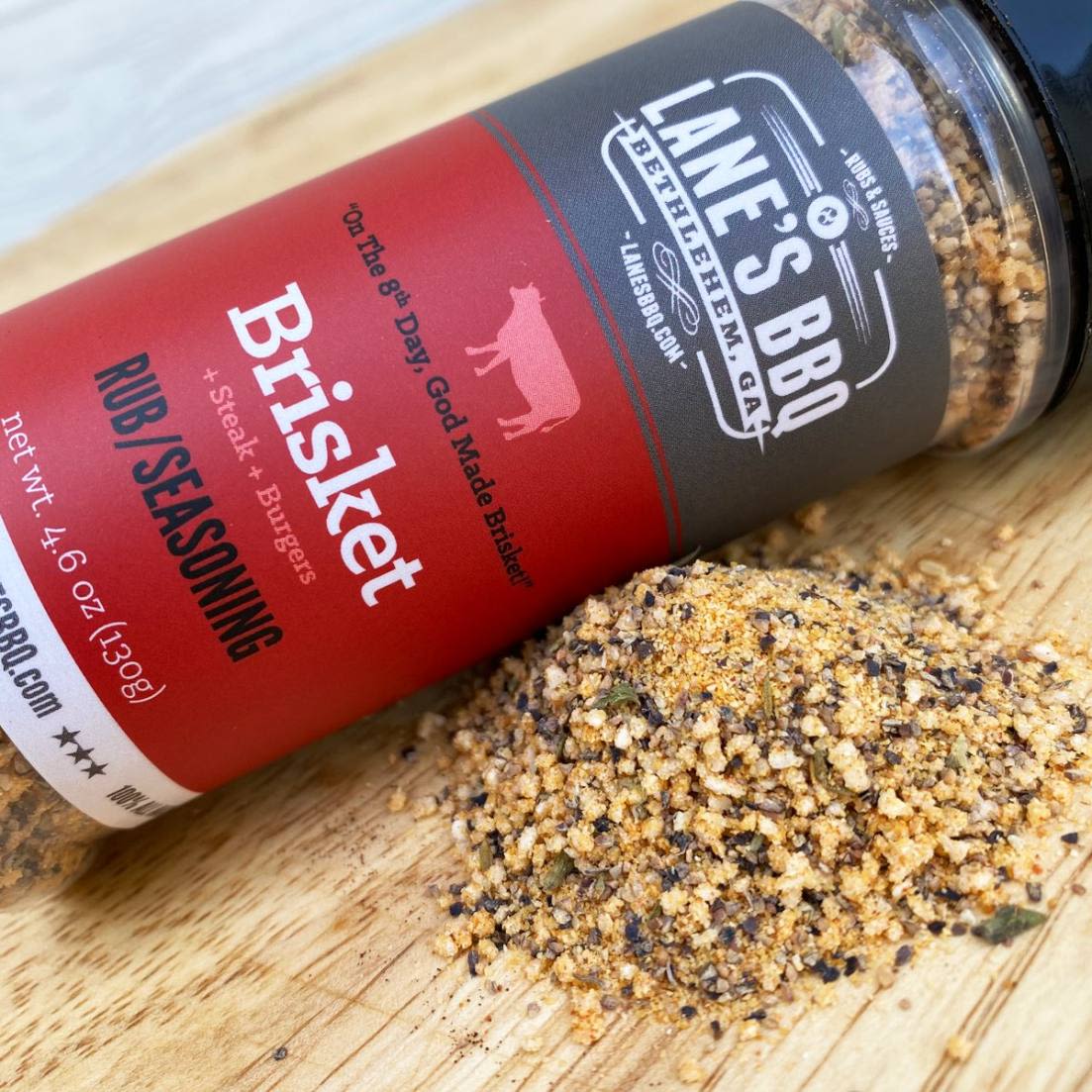Clear plastic bottle of Lane's Brisket Rub with black lid, seasoning spilled on wooden surface in grilling spices collection under $50