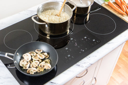 Induction cooktop with five cooking zones, digital controls, and pots cooking rice and sautéing mushrooms on countertop