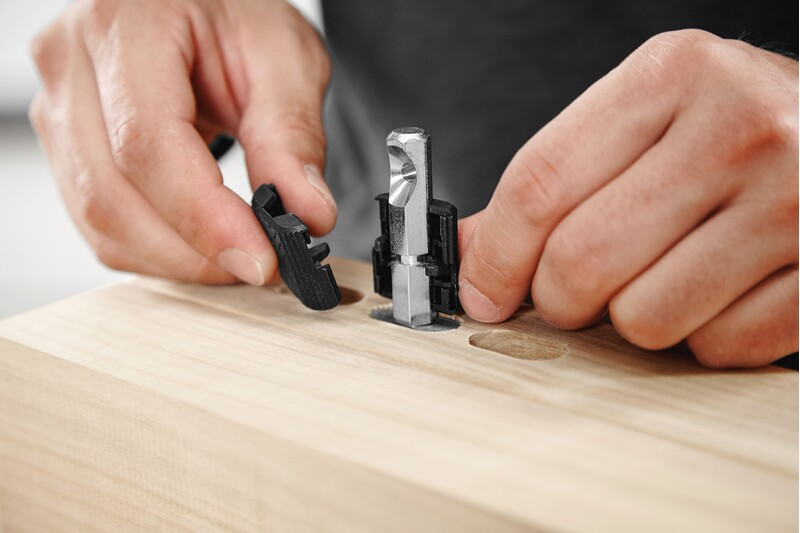 Hands installing a metal and plastic anchor bolt into wood for woodworking tool accessories and home improvement