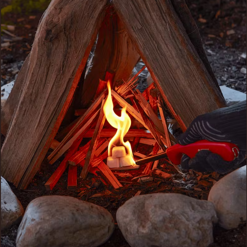 Outdoor firewood arranged in a teepee shape with flame igniting an odorless fire starter cube for grilling accessories.