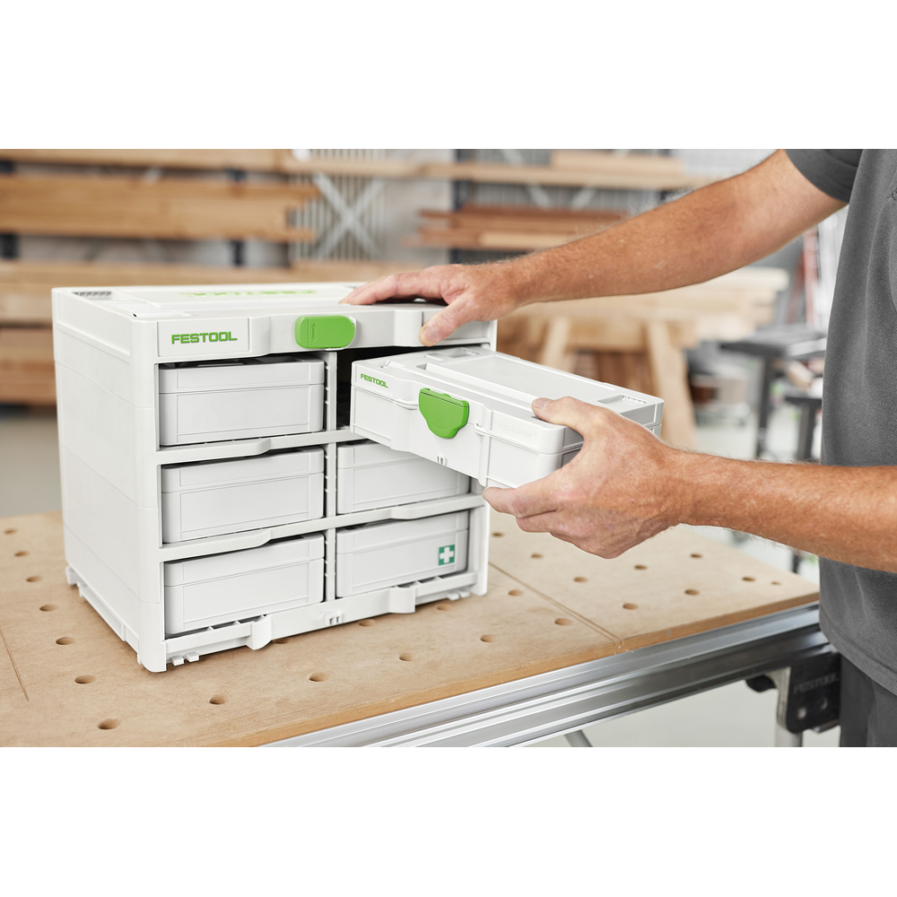 Person removing compact white and green Festool accessory case from modular storage unit in woodworking workspace
