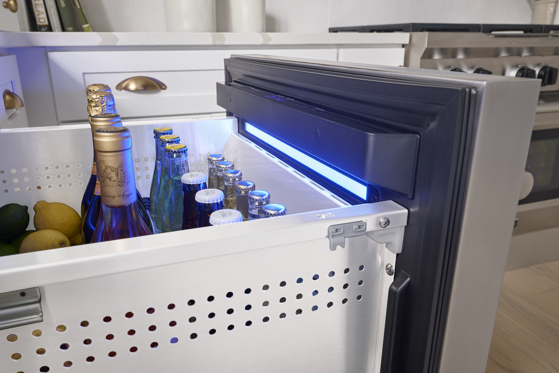 Under-counter stainless steel refrigerator drawer with chilled beverages and produce in modern kitchen setting