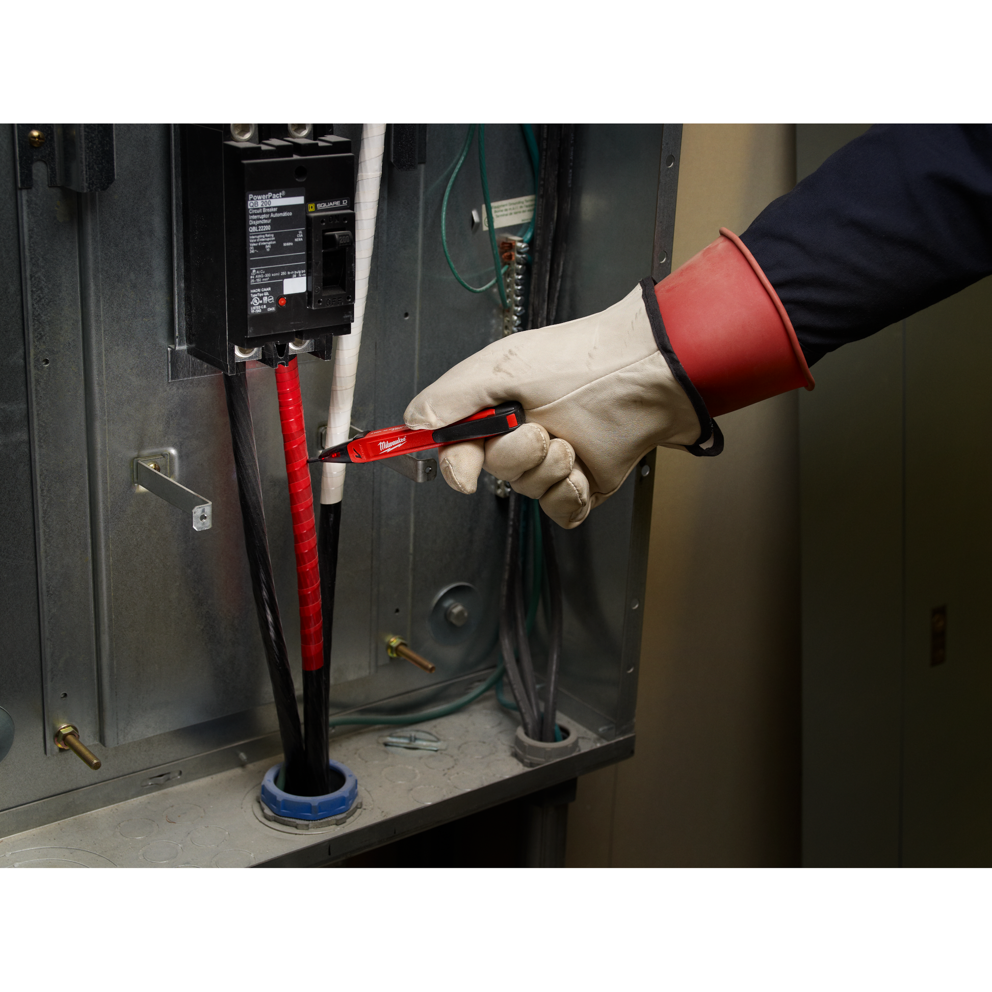 Red Milwaukee voltage detector held by gloved hand testing wires inside electrical panel for tools and home improvement use