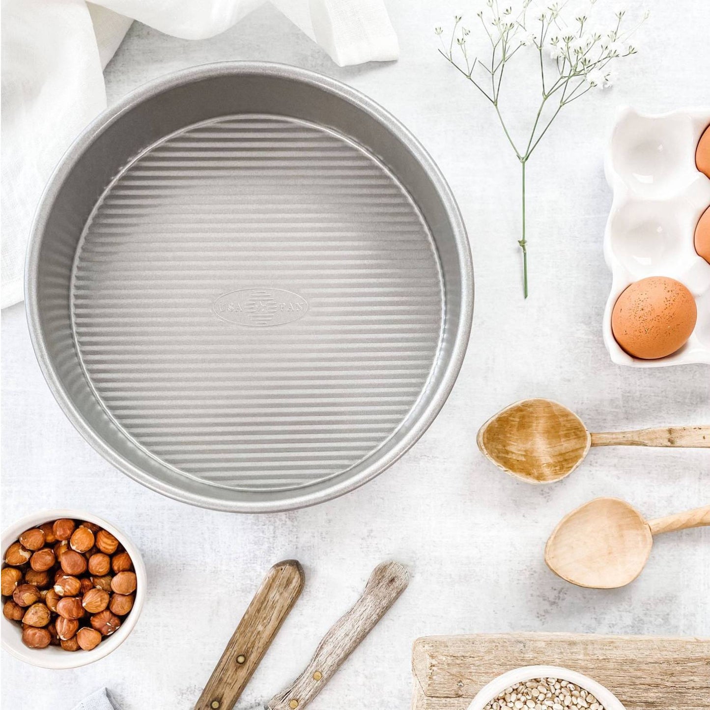 9-inch round baking pan with ridged interior surface surrounded by wooden spoons, eggs, and nuts for kitchen use