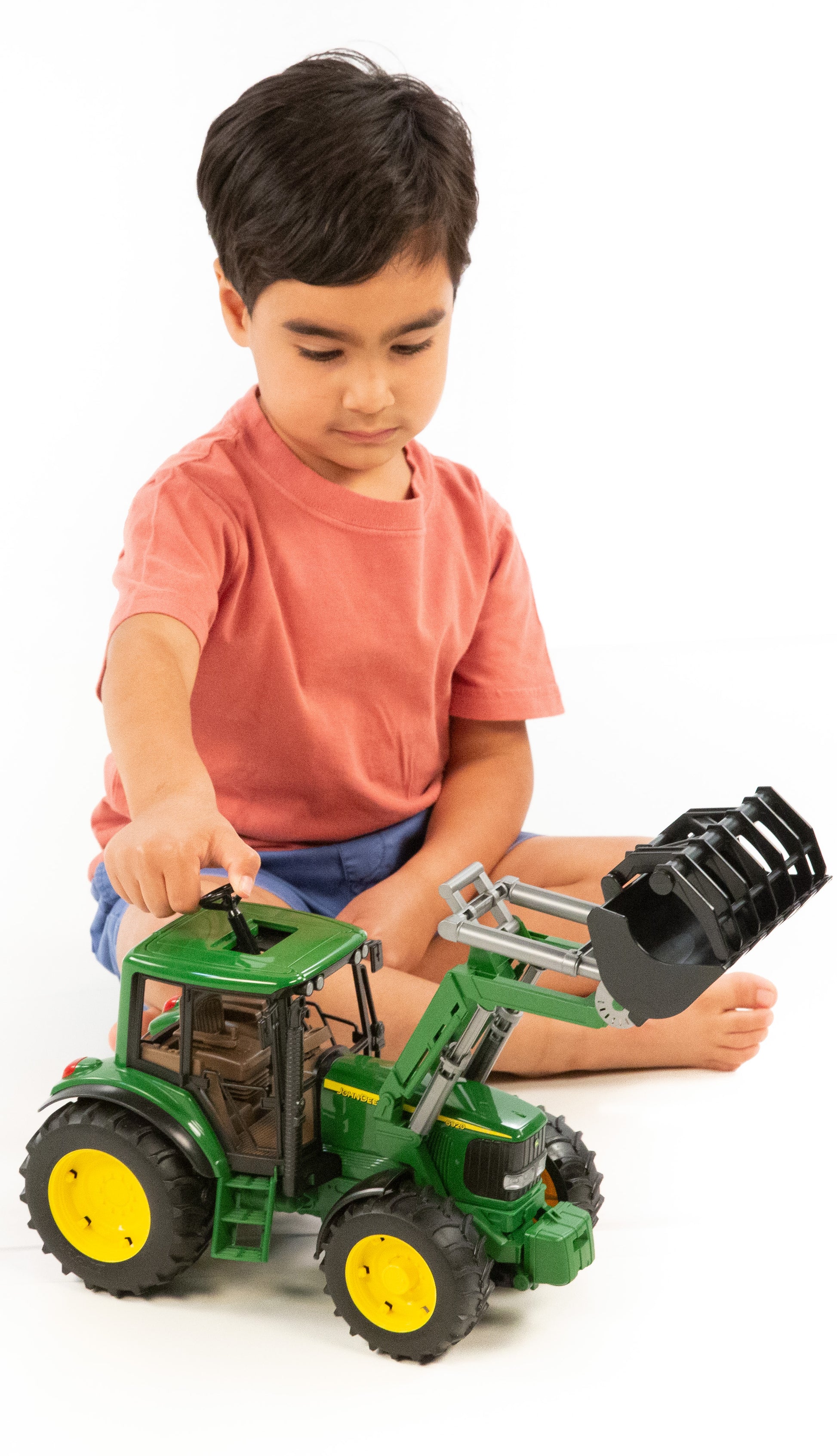 Child in red shirt playing with detailed green and yellow tractor toy featuring a functional frontloader bucket attachment