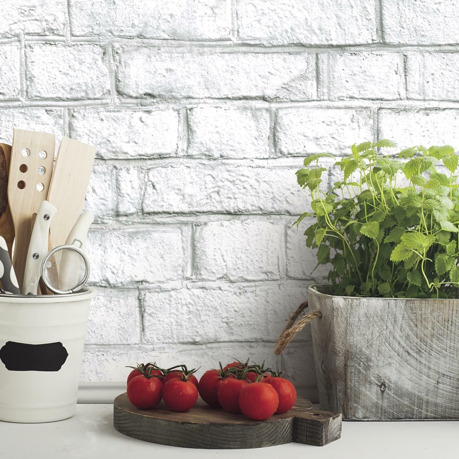 Whitewashed brick wall with kitchen utensils, fresh tomatoes on wooden cutting board, and potted herb plant nearby