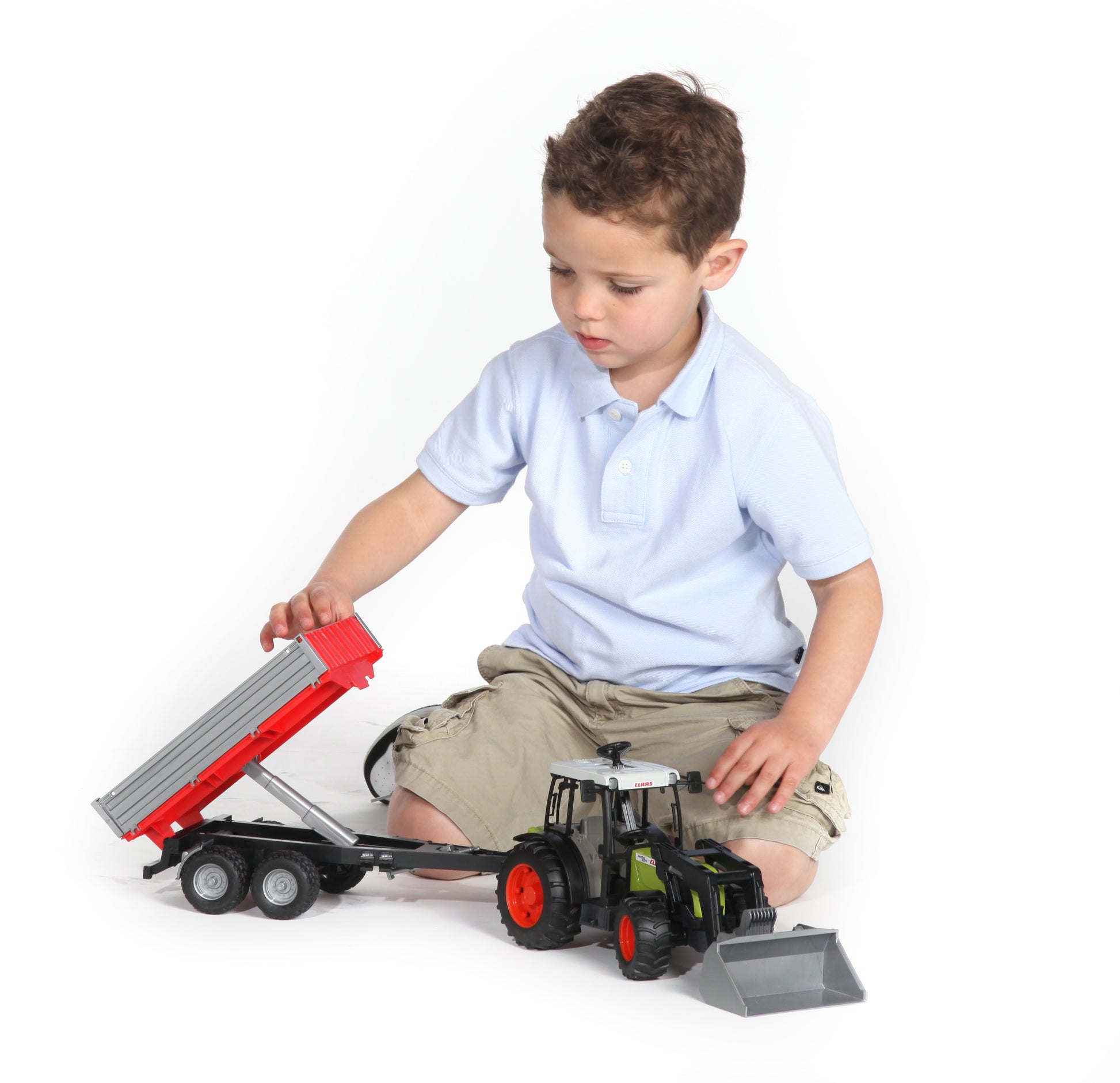 Child sitting on floor playing with Bruder CLAAS model tractor and red tipping trailer toy set