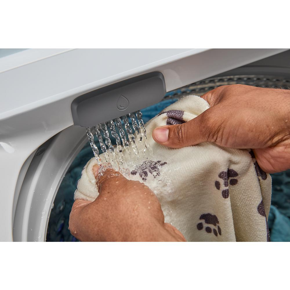 Hands rinsing a paw print patterned fabric under running water from the built-in washer faucet in a laundry appliance setting
