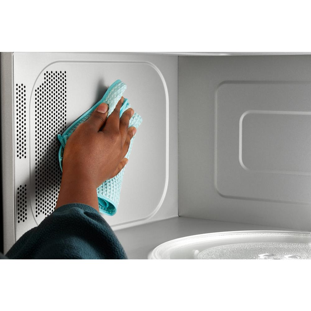 Hand wiping the smooth interior of a microwave with a blue cloth in kitchen and appliances setting