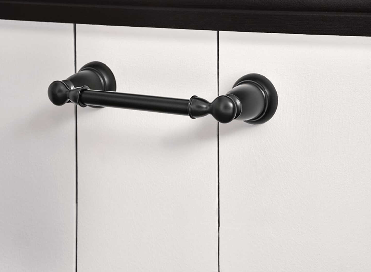 Moen Banbury Matte Black Toilet Paper Holder mounted on white paneled wall for home improvement use.