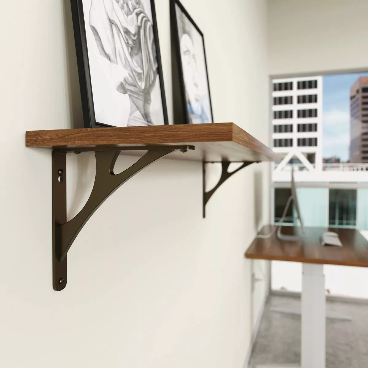 Bronze-finished metal shelf brackets supporting a wooden shelf with framed artwork in a modern office space
