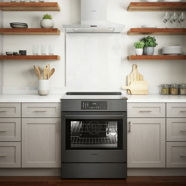 Black stainless steel induction slide-in range with digital touch controls in a bright modern kitchen setting