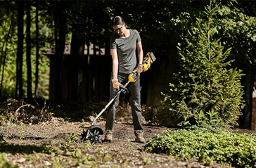 Person operating DEWALT cultivator attachment with steel tines in garden setting from Dewalt Outdoor Power Tools collection