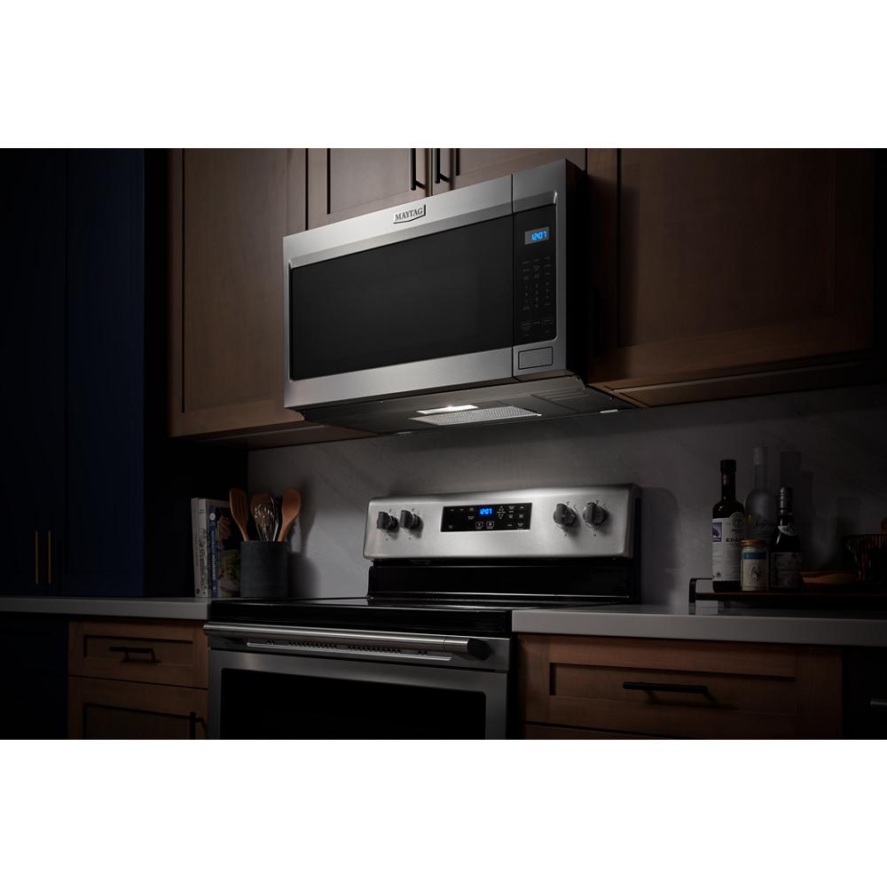 Stainless steel over-the-range microwave with digital display installed above matching electric stove in kitchen setting