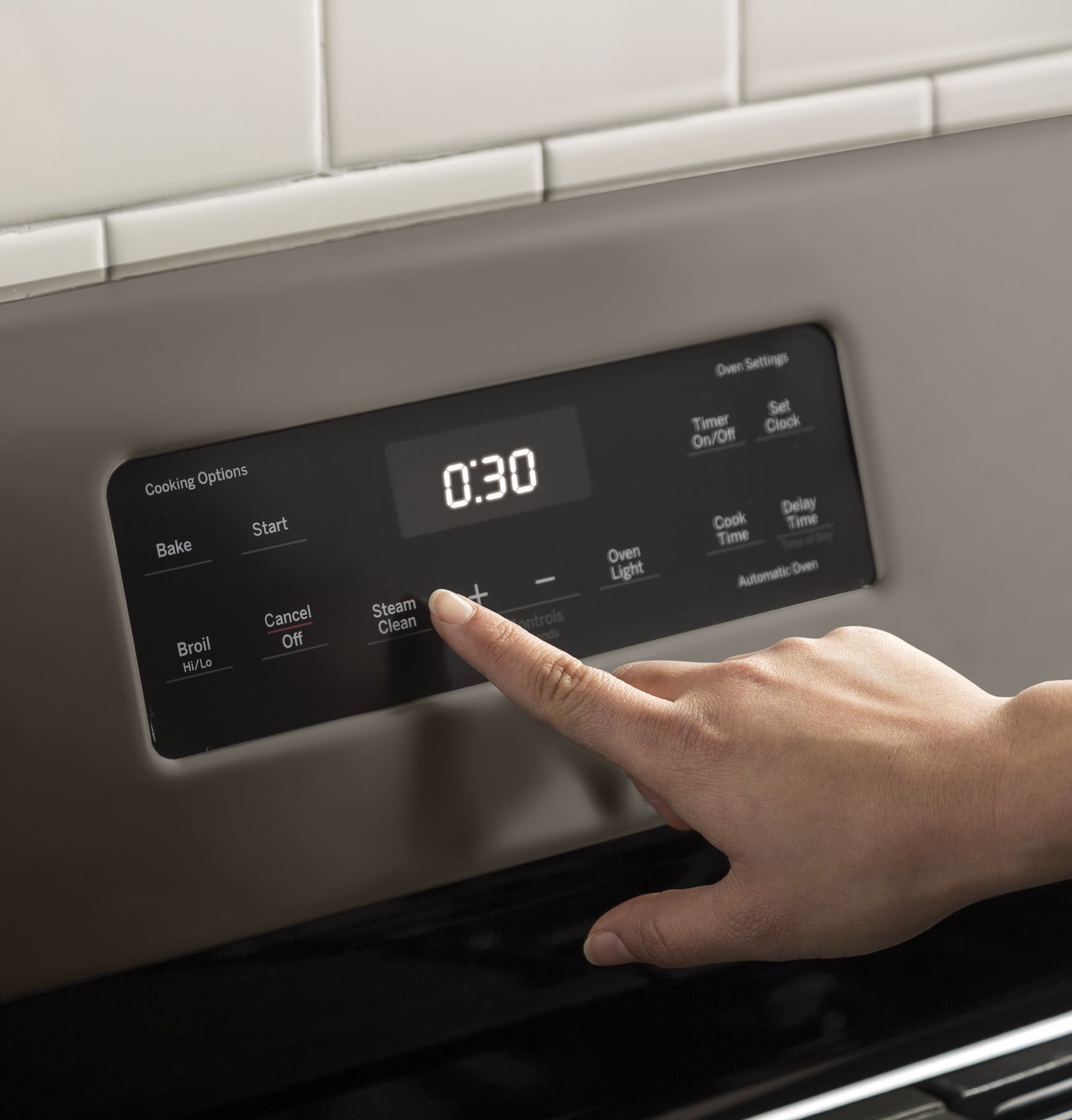 Finger pressing the steam clean button on the digital control panel of a stainless steel gas range in a kitchen setting