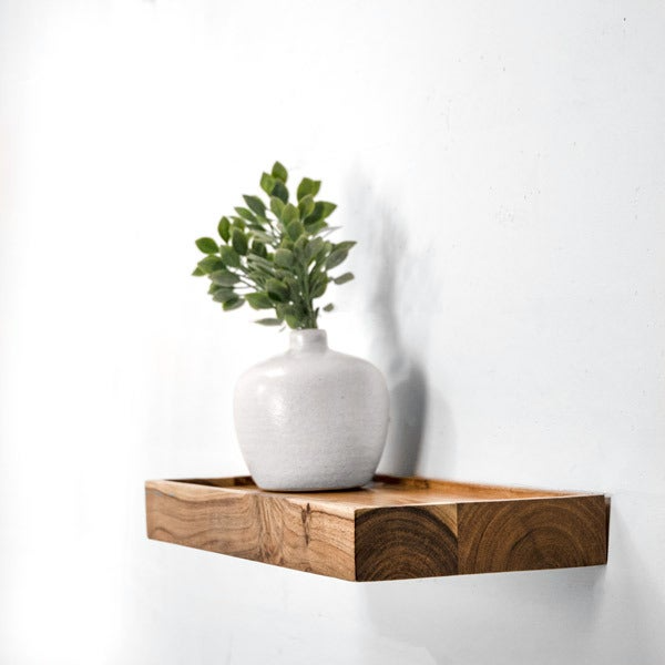 Floating wood shelf with natural rustic finish holding a small white ceramic vase with green foliage in a bathroom setting