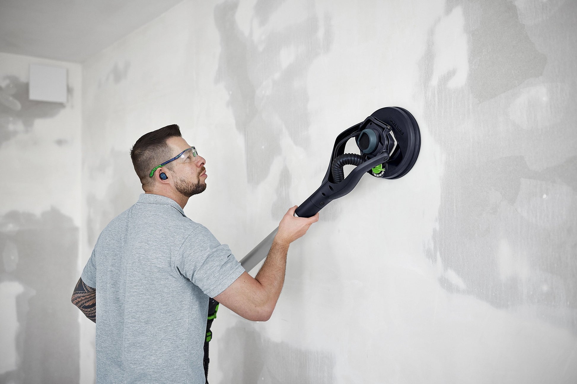 Man wearing safety glasses using a drywall sander on a patched wall in a home improvement setting