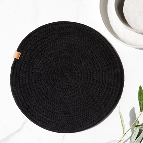 Black round woven placemat with small tan tag, styled with white ceramic dishes for home and garden use
