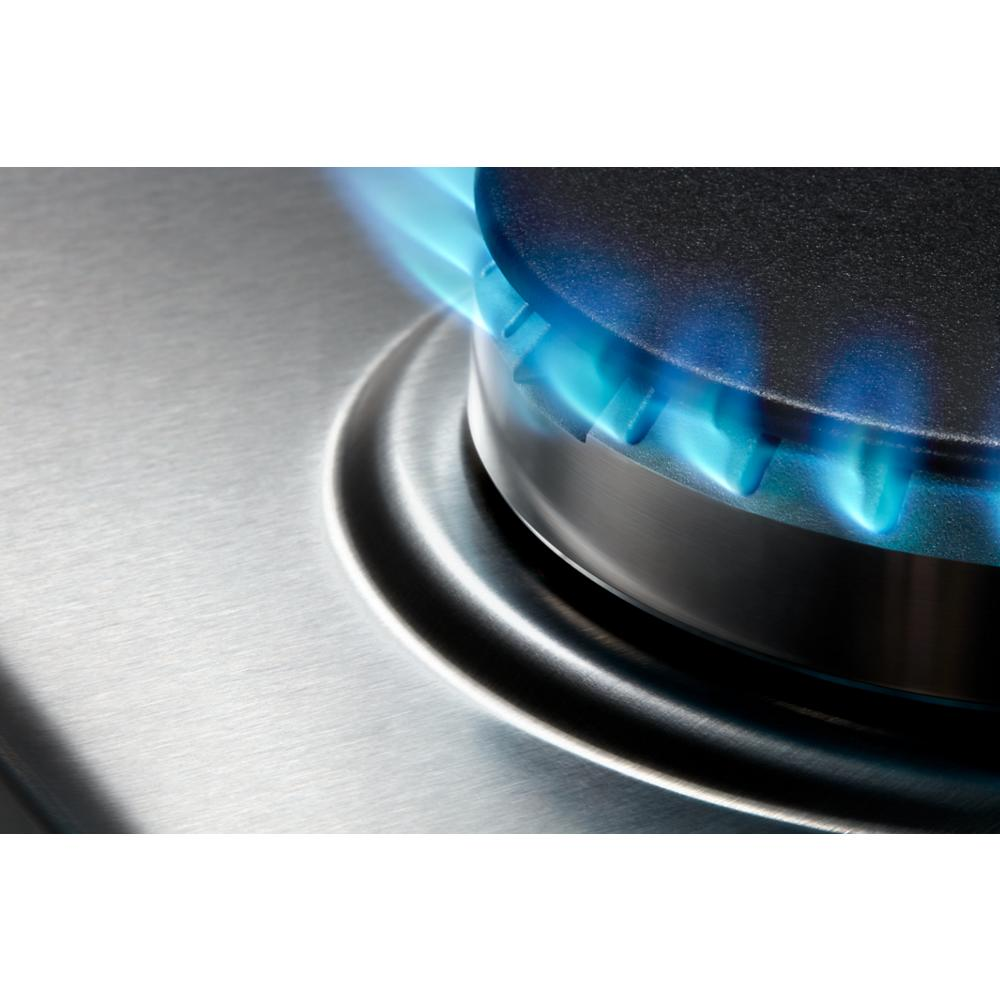 Close-up of blue flame burning around cast-iron burner cap on stainless steel cooktop surface for home kitchen