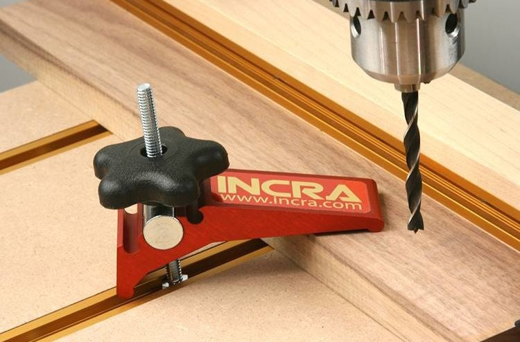 Red and black INCRA Build-It Clamp securing wood for precise drilling in woodworking hand tools and measuring tools collections