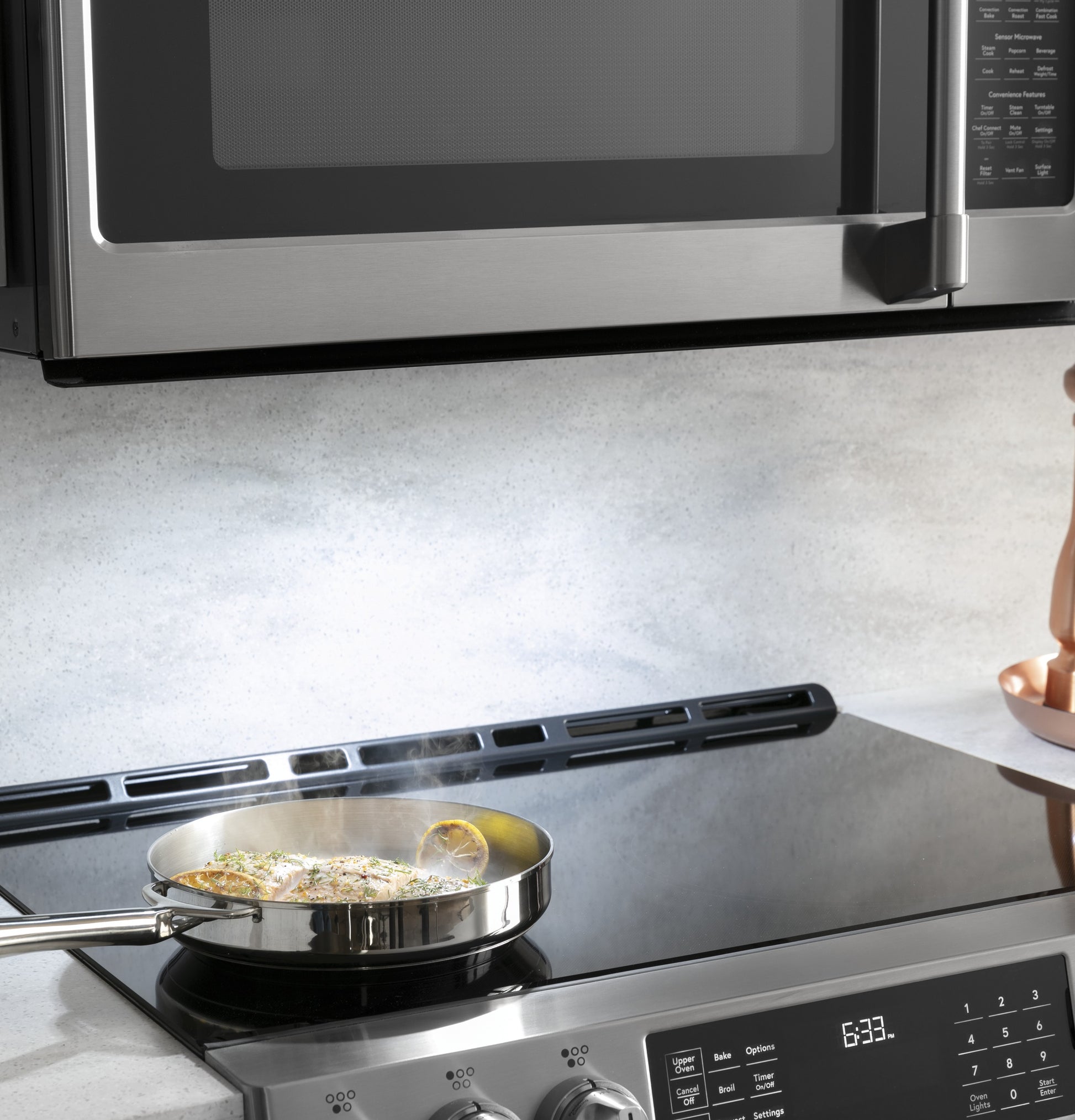 Stainless steel microwave installed above modern electric stove with frying pan cooking in kitchen appliances setting