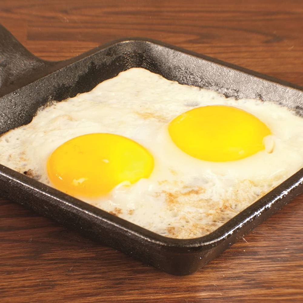 Square cast iron skillet cooking two sunny side up eggs on wooden surface in kitchenware under $50 collection