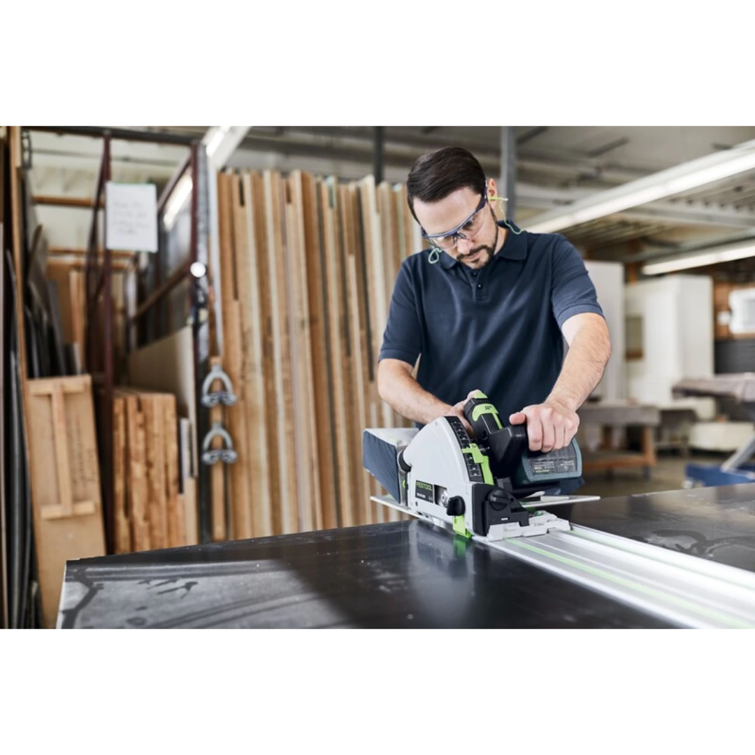 Man wearing safety glasses operating a circular saw on a Festool guide rail in a woodworking shop environment