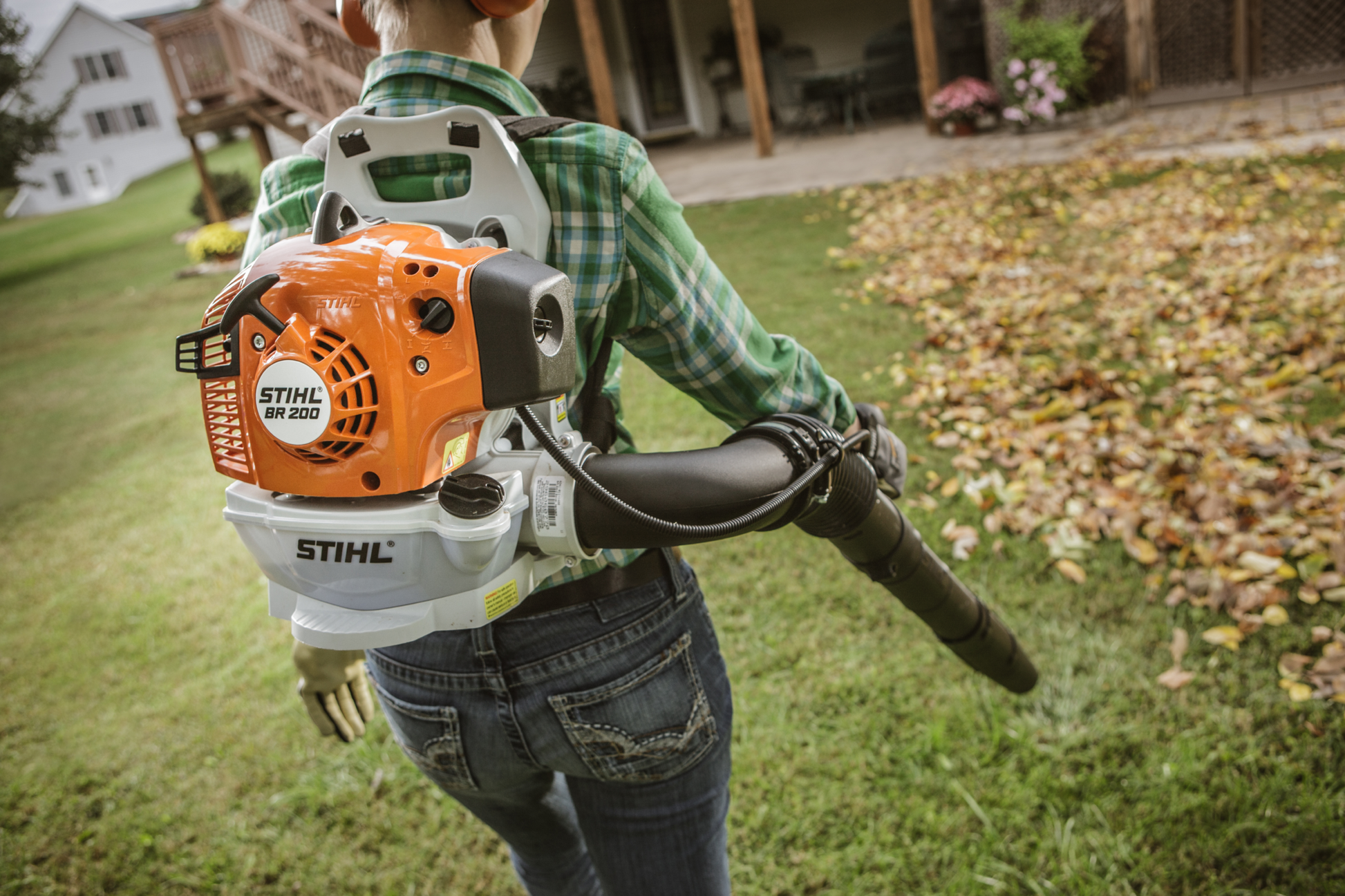 Person using a STIHL BR 200 Lightweight Backpack Blower to clear fallen leaves from a grassy lawn area